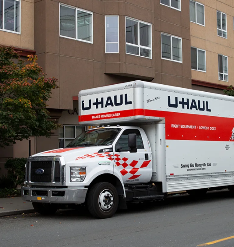 Camion de déménagement U-Haul stationné dans la rue devant un complexe d’appartements.